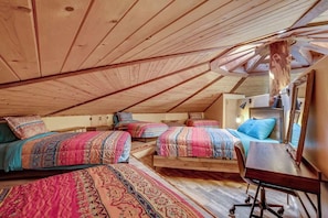 Une chambre aménagée en mezzanine avec trois lits, un bureau en bois et un plafond en pente.