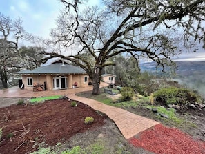 Ein Haus mit befestigter Auffahrt, einem großen Baum und Blick auf die Landschaft.