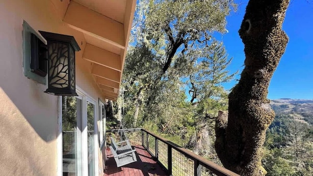 Une terrasse en bois avec une rambarde, un fauteuil suspendu et une vue sur un paysage montagneux.