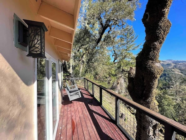 A wooden deck with a railing, a hanging chair, and a view of a mountainous landscape.