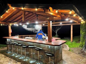 Un bancone all'aperto con struttura in legno, sgabelli da bar e una griglia.