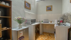 Eine kleine Küche mit Mikrowelle, Spüle und einem Herd. Ein Holzboden, an der Wand ein Regal mit Geschirr und eine Vase mit Blumen. Die Wände sind in einer hellen Farbe gehalten.