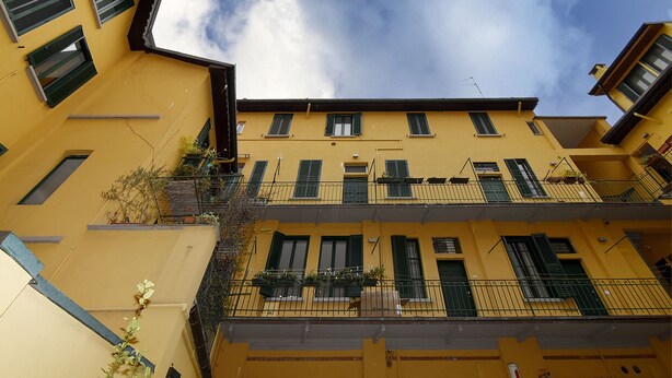 A yellow building with multiple balconies, green shutters, and a clear sky.