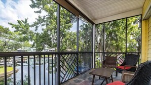 A covered balcony with wicker furniture and a view of a water body and trees. - Bigfoot Bungalow -Enjoy being directly on clear waters of the Weeki Wachee River (Weeki Wachee)