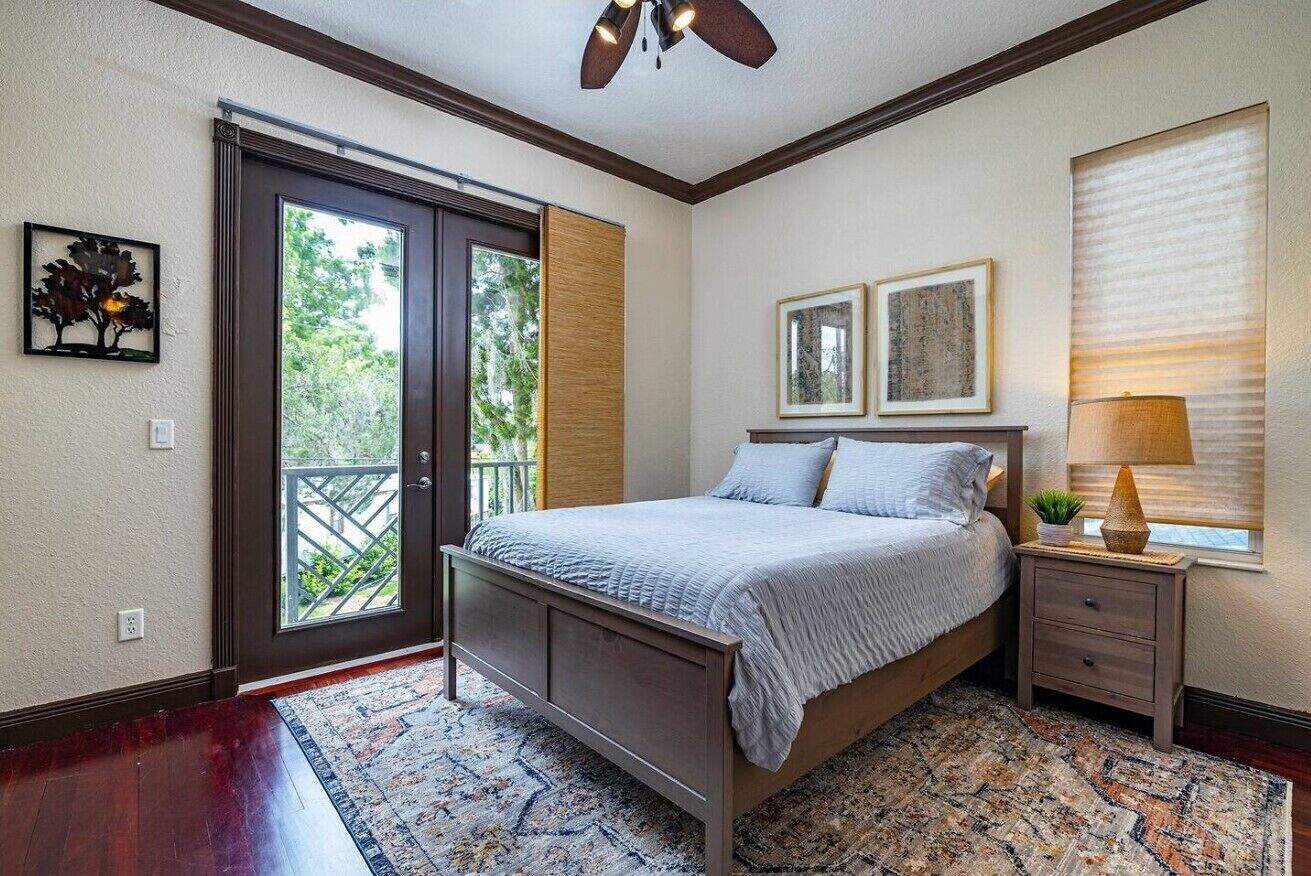 A bedroom with a bed, a nightstand, a window with blinds, and a door leading to a balcony.