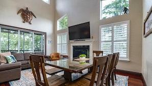 A spacious living room with a fireplace, a large flat-screen TV, a dining area with wooden chairs, and a sofa with a patterned rug. - Bigfoot Bungalow -Enjoy being directly on clear waters of the Weeki Wachee River (Weeki Wachee)