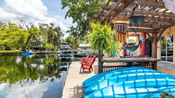 A poolside area with a wooden pergola, a welcome sign, and a seating area with red chairs. - Bigfoot Bungalow -Enjoy being directly on clear waters of the Weeki Wachee River (Weeki Wachee)