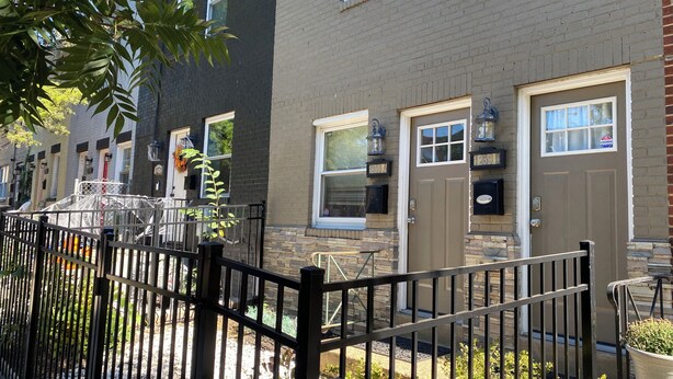 A row of townhouses with a black metal fence, stone accents, and a clear sky.