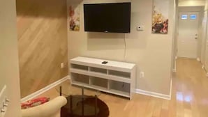 A room with a flat-screen TV mounted on the wall, a white entertainment unit below it, and a wooden floor.