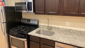A kitchen with a gas stove, oven, microwave, stainless steel sink, and dark wooden cabinets.