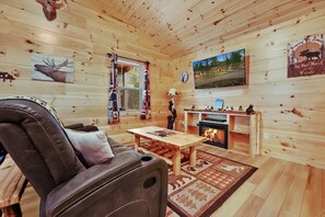 Ein gemütliches Blockhaus-Interieur mit einer Ledersofa, einem Holztisch, einem Kamin und Wandbildern, darunter ein Elch und eine aussichtsreiche Landschaft.