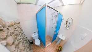 Moderni kylpyhuone, jossa on kiviseinä yhtenä seinänä, sininen suihkukaappi, wc-istuin ja pesuallas.