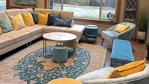 A living room with a sectional sofa, a round coffee table, a blue armchair, and a yellow ottoman.