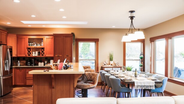 A modern kitchen with wooden cabinets, a central island, and a dining area with a table and chairs.
