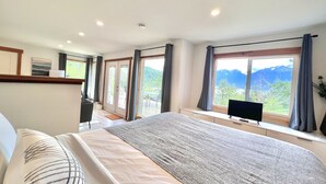 A bedroom with a large bed, a TV, and a view of mountains through the window.