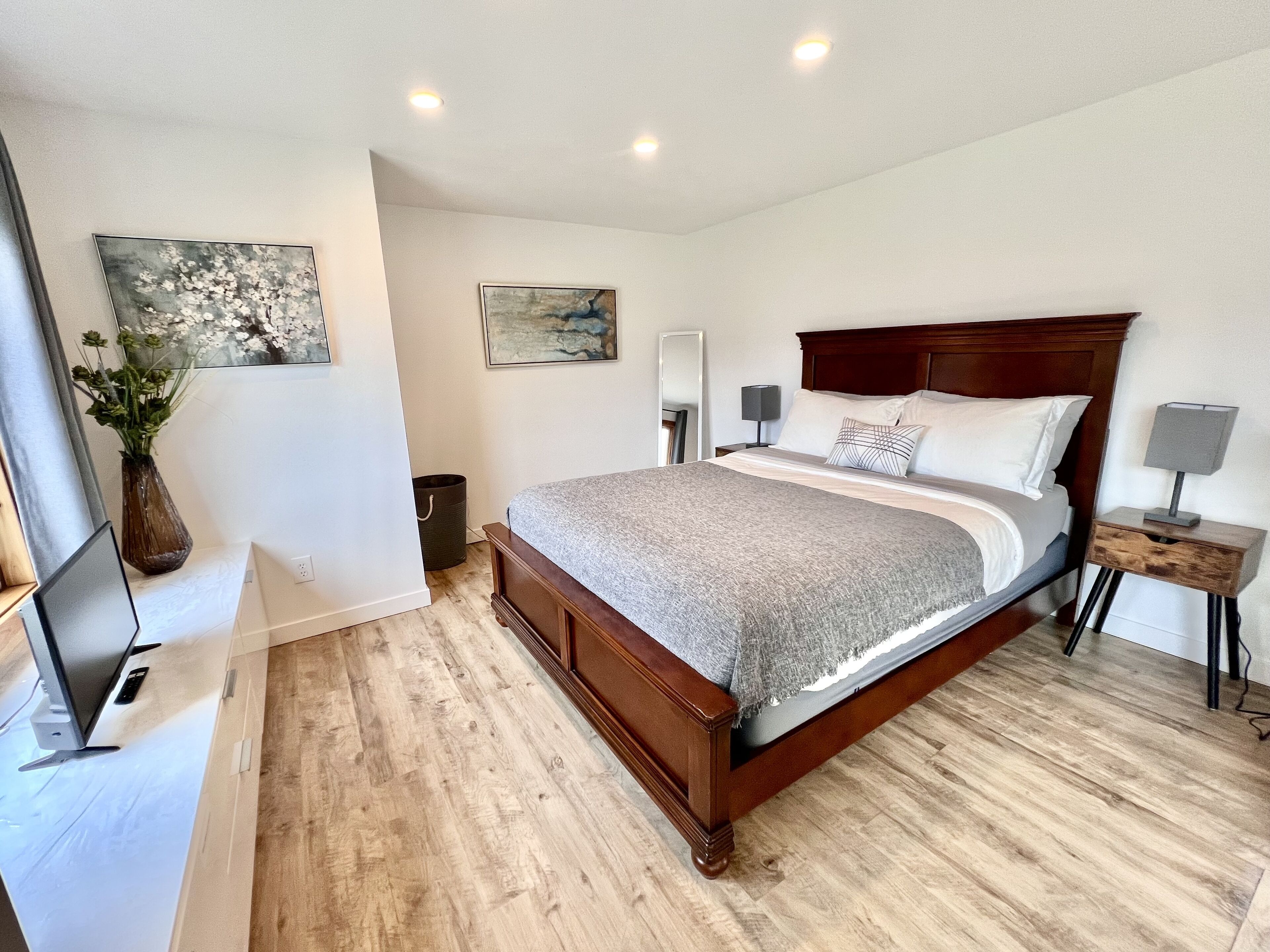 A bedroom with a wooden bed, bedside tables, a desk with a computer, and artwork on the walls.