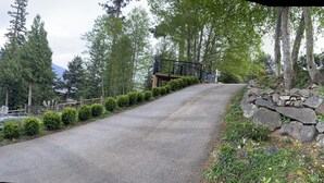 A residential driveway leading to a house with a garage, surrounded by trees and a mountainous backdrop.
