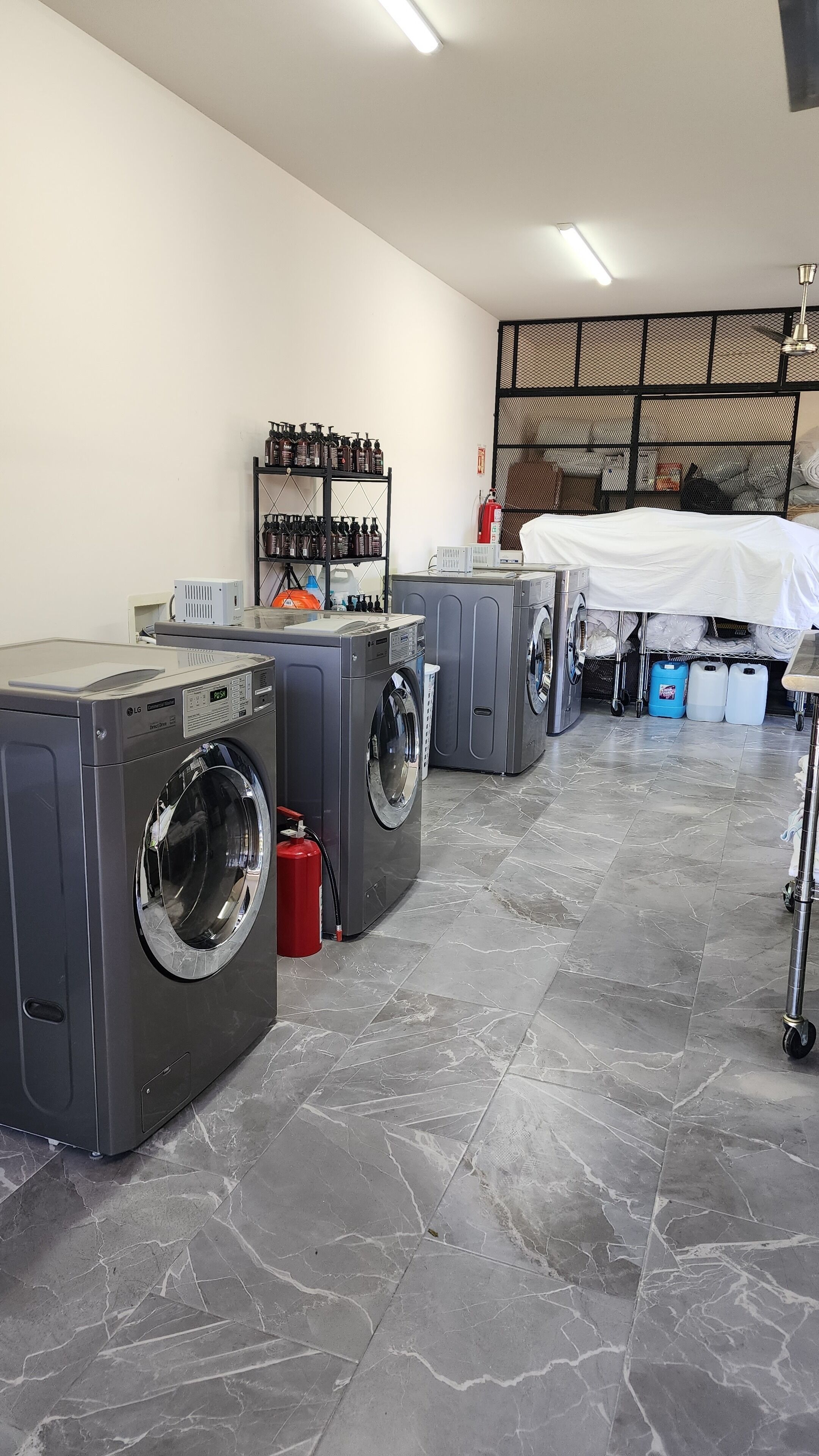 A laundry facility with multiple washing machines, a shelf with bottles, and a fire extinguisher.