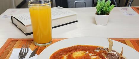 Une table à manger avec une assiette de nourriture, un verre de jus d’orange et un livre.