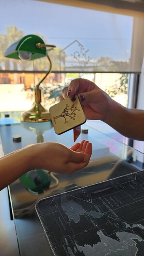 A hand holding a wooden keychain with a tree design, being handed over to another hand. - SUITES LOMBOY & PLAZA (San José del Cabo)
