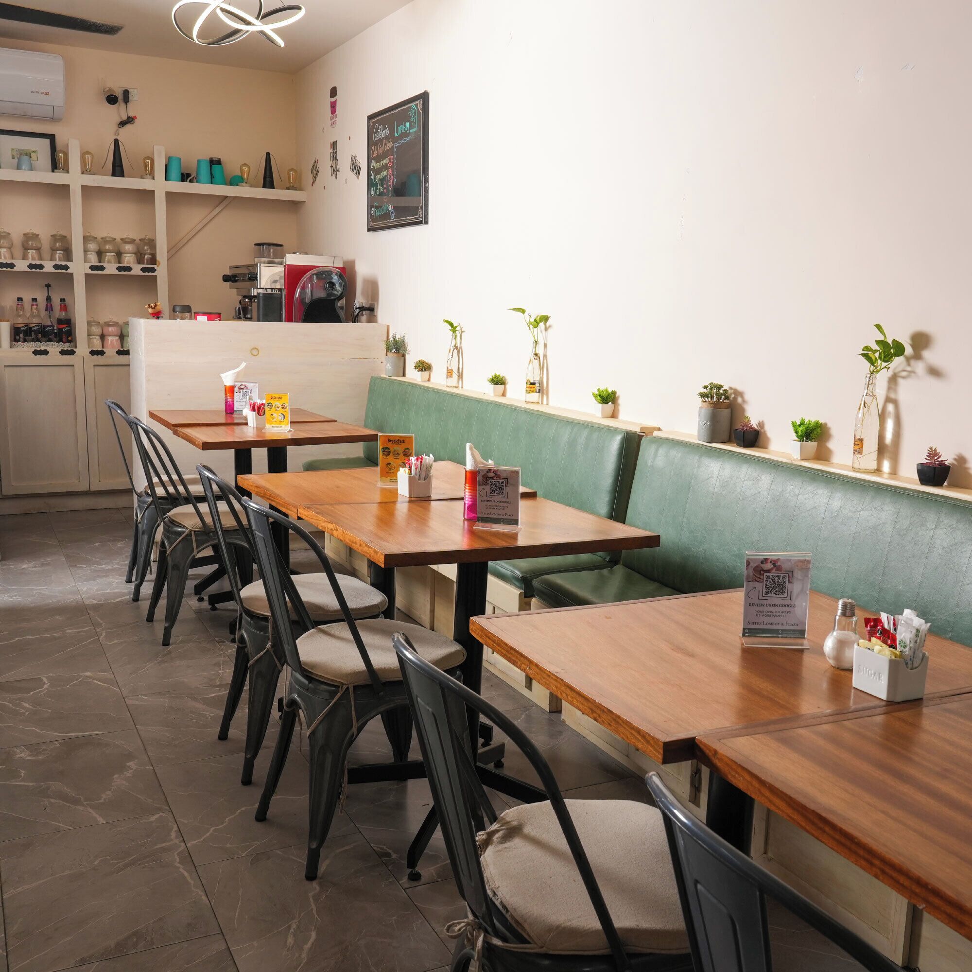 Restaurante com mesas e cadeiras de madeira, área de assentos em cabine verde e diversas plantas em prateleiras.