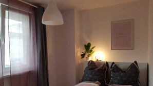 Een slaapkamer met een bed, twee kussens, een bedlampje, een plant en een fotokader aan de muur.