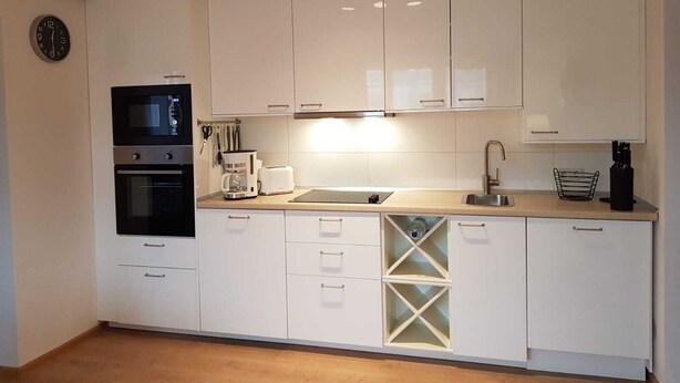 Een moderne keuken met witte kastjes, een inbouwoven, een koffiezetapparaat en een spoelbak.