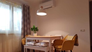 Een eethoek met een tafel, stoelen, een bank, een potplant en een airconditioning.