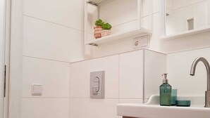 Een badkamer met toilet, wastafel met spiegel en een plankje met een plant.