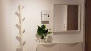 Een gang met een witte kast, een potplant, een sleutelhouder aan de muur en een spiegel.