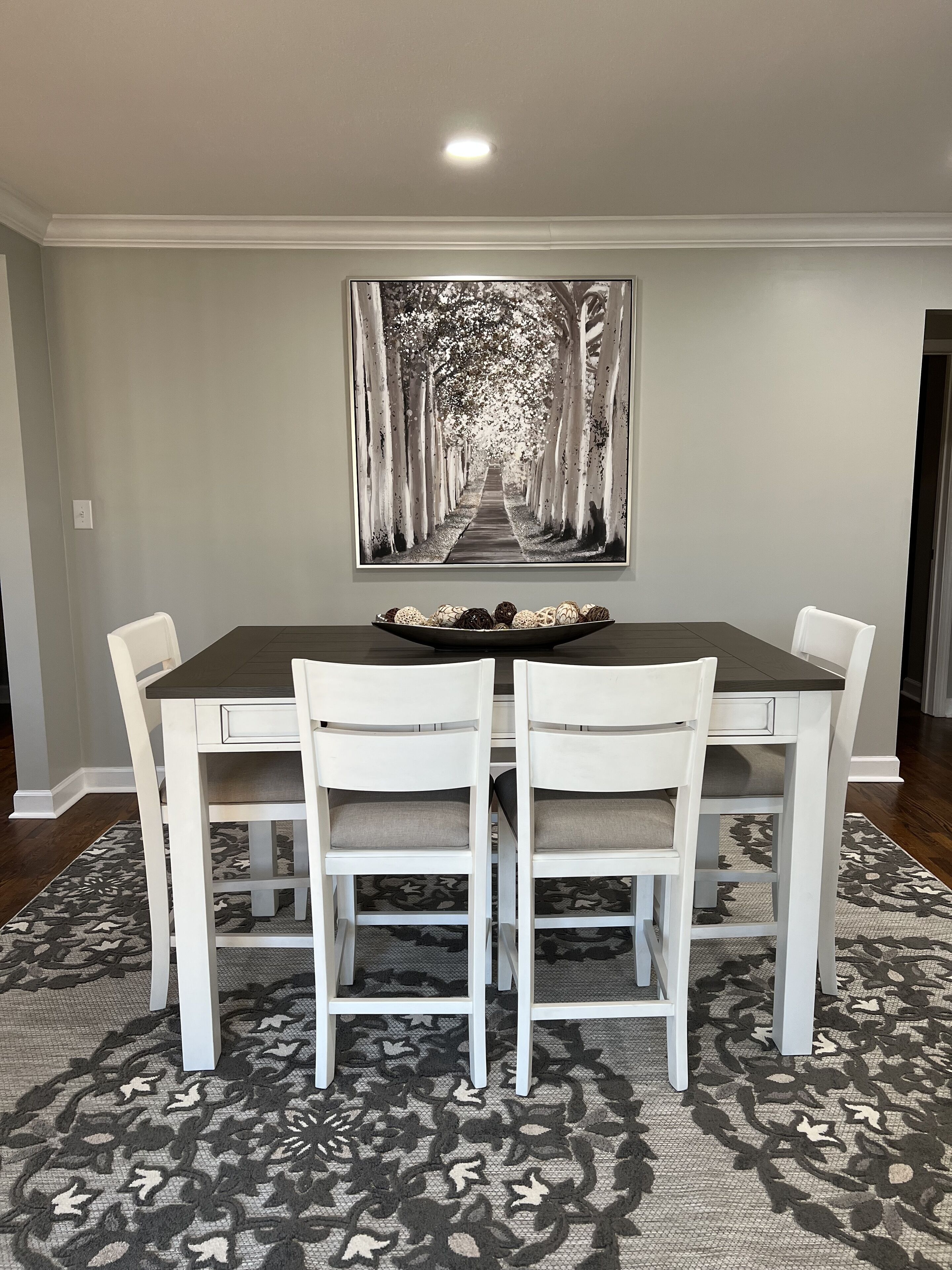 Une salle à manger avec une table en bois foncé, des chaises blanches et un tapis à motifs.