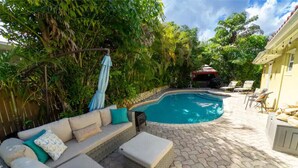 Ein Garten mit Pool, überdachter Grillplatz und Sitzgelegenheit im Freien.