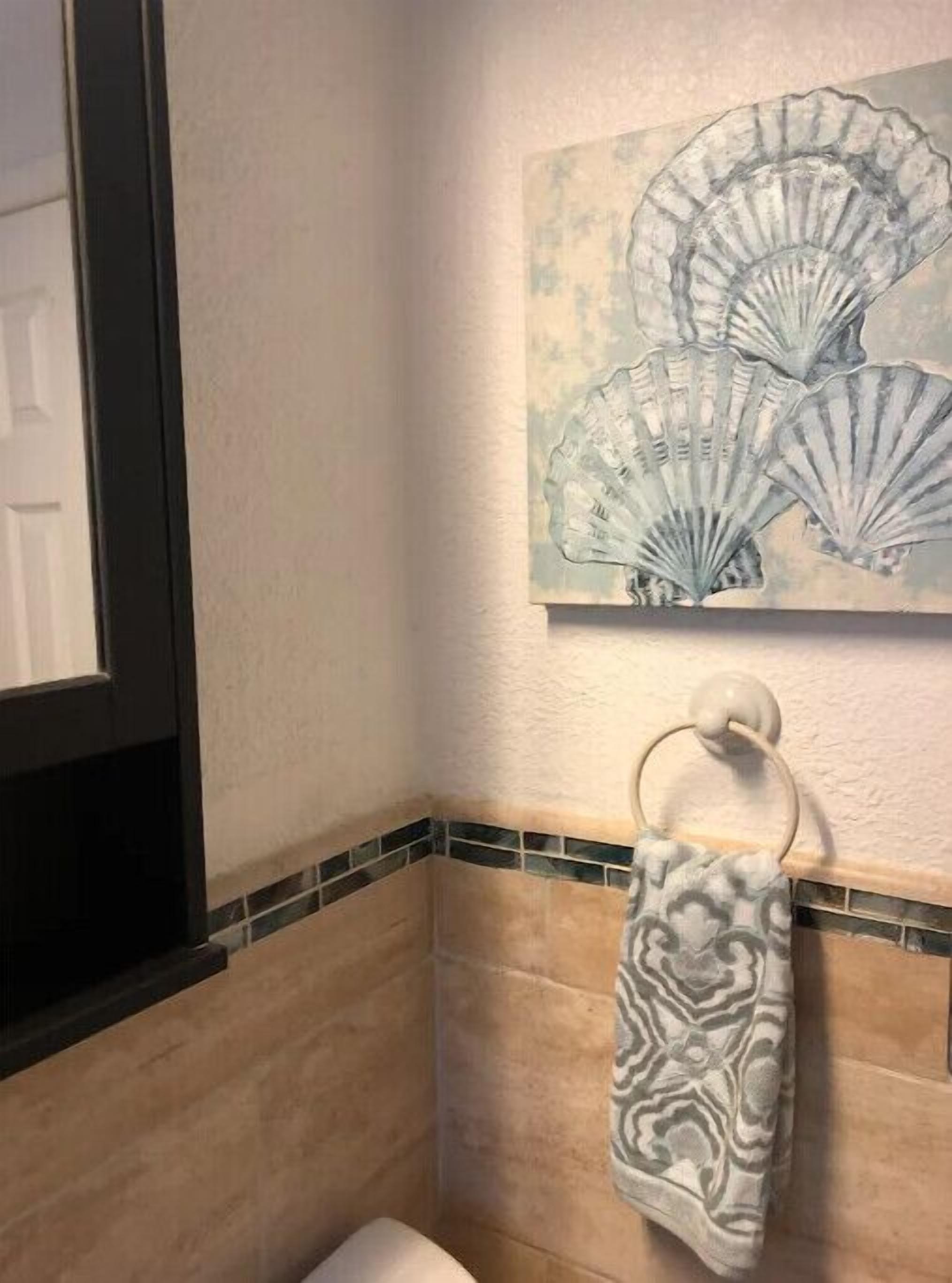 A bathroom with a tiled wall, a towel rack, and a painting of seashells.