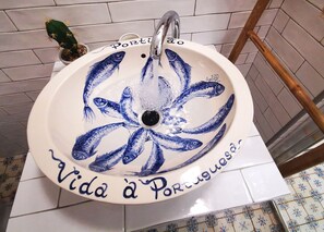 A bathroom sink with a decorative design featuring fish and the text "Vida à Portuguesa".