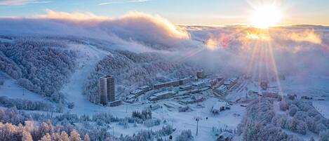 A snow-covered ski resort with multiple buildings, including a tall hotel, and a ski lift.