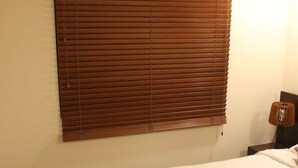 Een slaapkamer met een groot bed, houten jaloezieën, een nachtkastje en een wandlamp.
