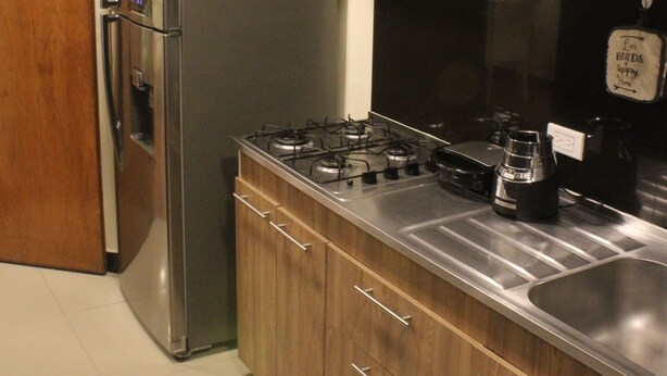 Een keuken met een roestvrijstalen koelkast, houten kastjes, een gasfornuis en een spoelbak.