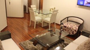 Een woonkamer met een glazen salontafel, een bank en een eettafel met stoelen.