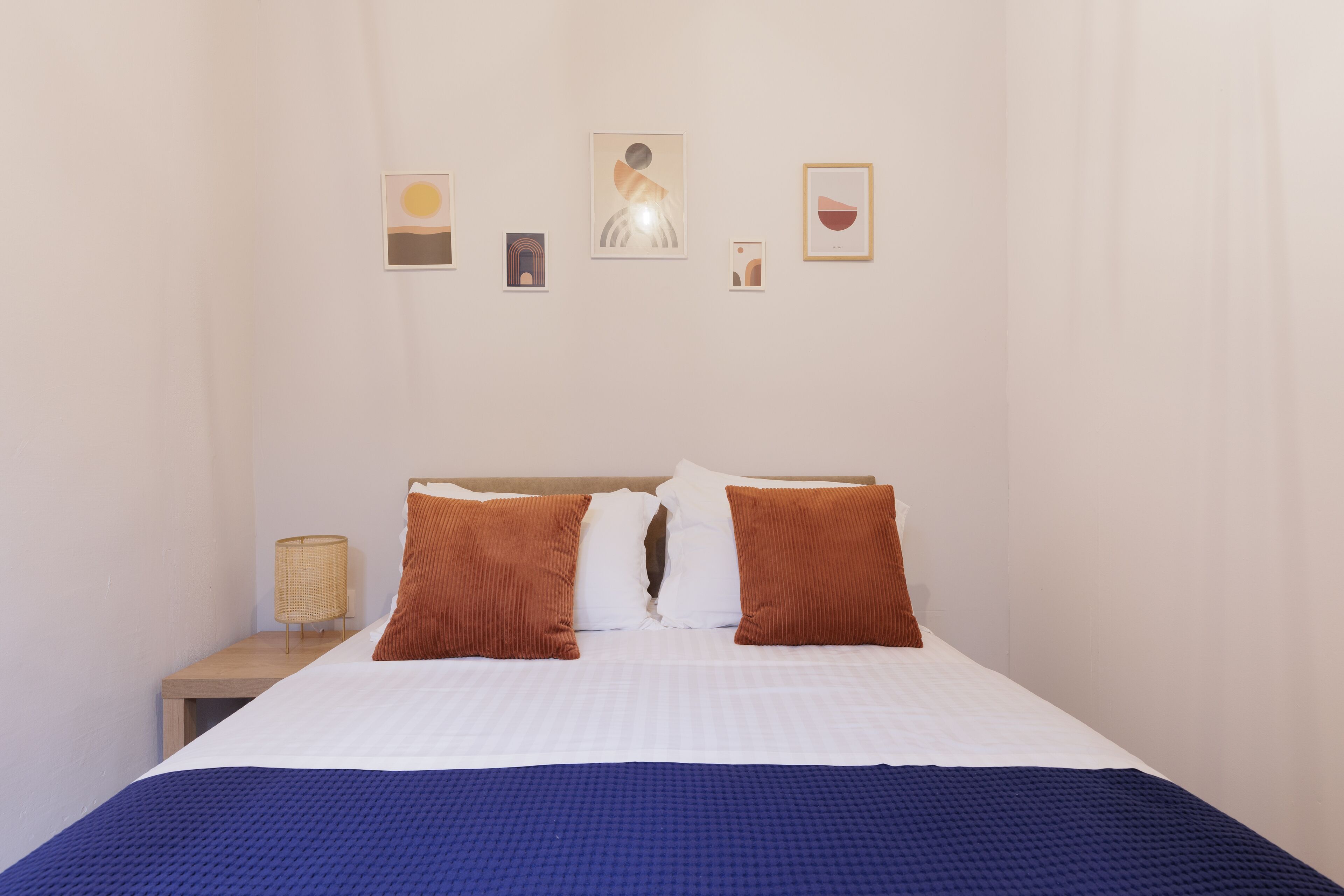 A neatly made bed with a blue blanket, two brown pillows, and a white comforter. There are four framed artworks on the wall above the bed.