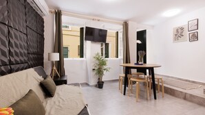 Quarto de hotel moderno com cama, mesa de jantar com cadeiras, um vaso de planta e uma televisão de tela plana.