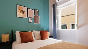 Uma cama bem arrumada com um edredom branco e marrom, parede verde-água e quadros na parede acima.