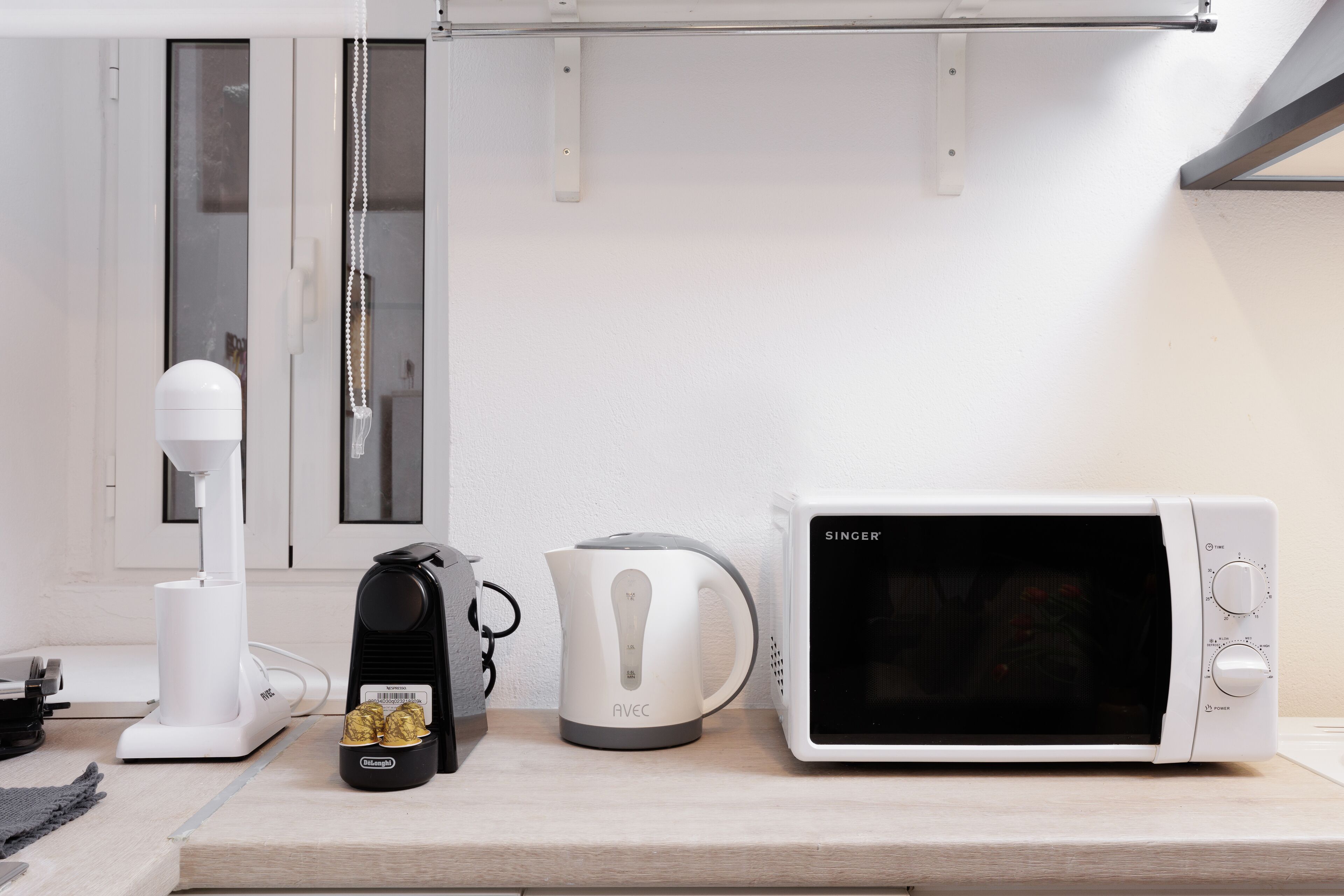 Una encimera de cocina con una cafetera blanca, un hervidor y un microondas.