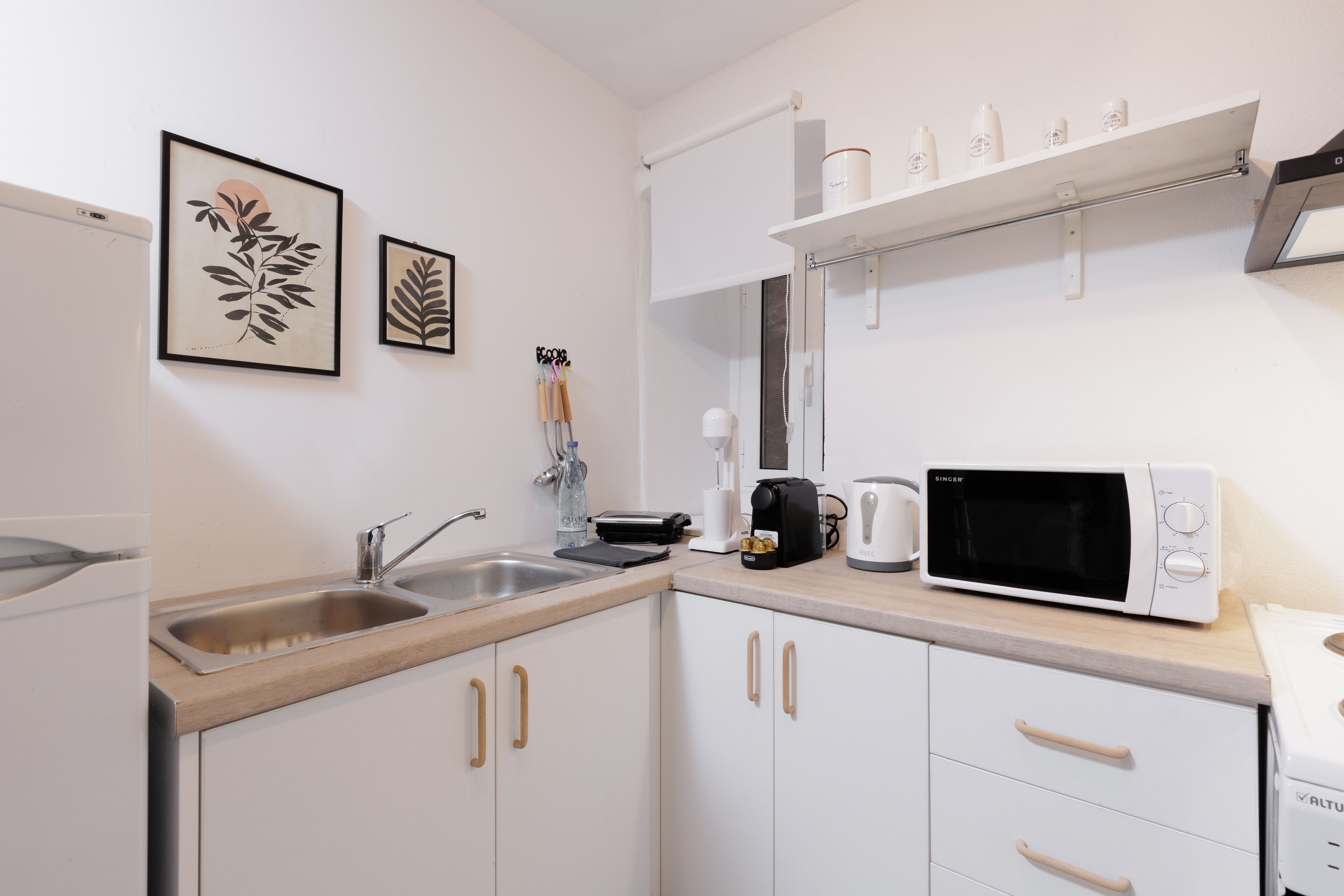 Cocina moderna con armarios blancos, pileta de acero inoxidable, microondas y cafetera.