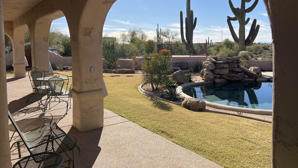 Une terrasse extérieure avec des chaises en métal et une petite piscine, entourée de cactus et de rochers.