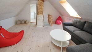 Un habitación tipo loft con techo inclinado, un sofá gris, un sillón de peluche rojo, una mesita de centro blanca y un tragaluz.