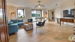 A spacious living room with a blue sofa, a dining table, and a TV. - Leocadie - Plenee Jugon (PLENEE JUGON)