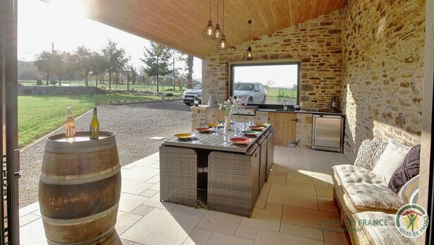 A rustic stone interior with a wooden ceiling, a stone wall, a bar area, and a seating area with a sofa. - Leocadie - Plenee Jugon (PLENEE JUGON)