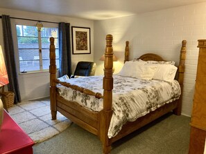 Un lit à baldaquin avec une couvre-lit à motifs floraux, une chaise, une lampe et un tableau encadré au mur.