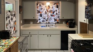 Una cocina con armarios blancos, una encimera, un fregadero, una estufa y una ventana con cortina estampada.