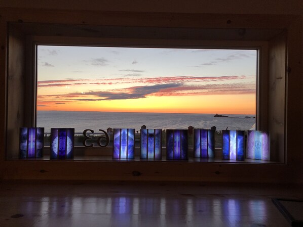 A room with a large window overlooking a sunset over the ocean.